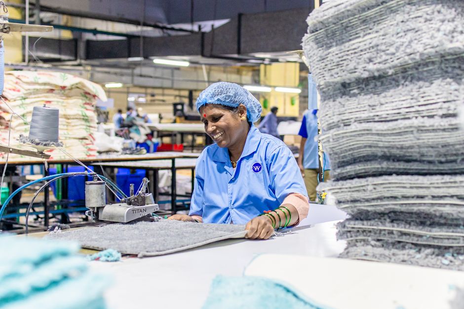 A cheerful textile worker operates machinery in a bustling factory environment.