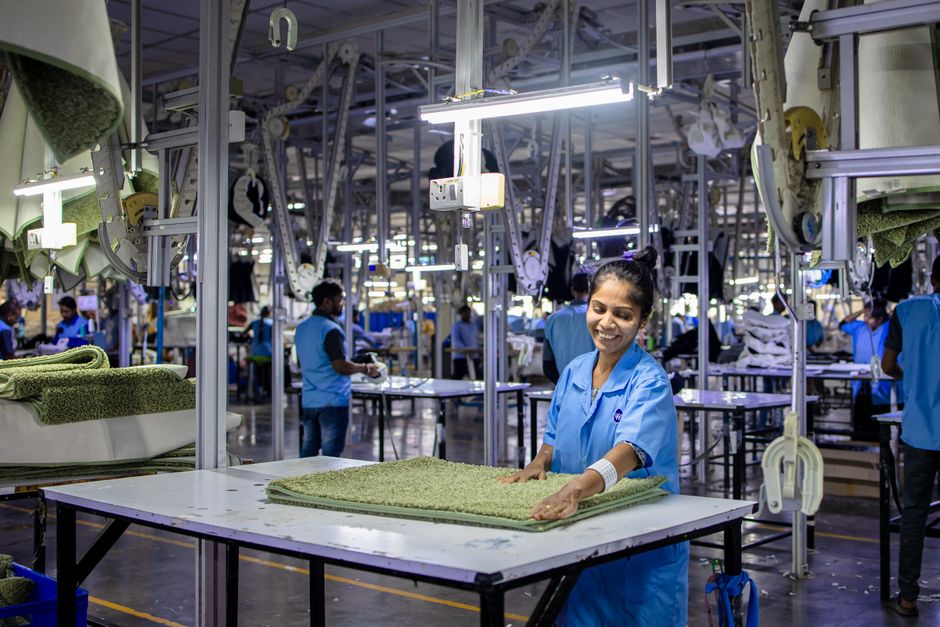 A cheerful factory worker arranges textiles in a well-lit manufacturing facility.