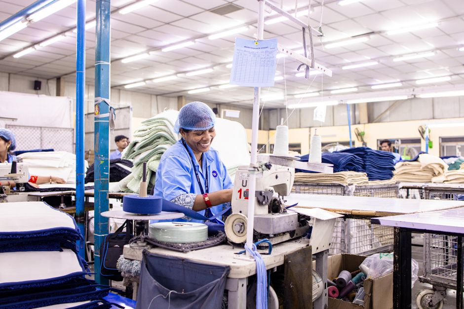 A cheerful female worker operates a sewing machine in a textile factory.
